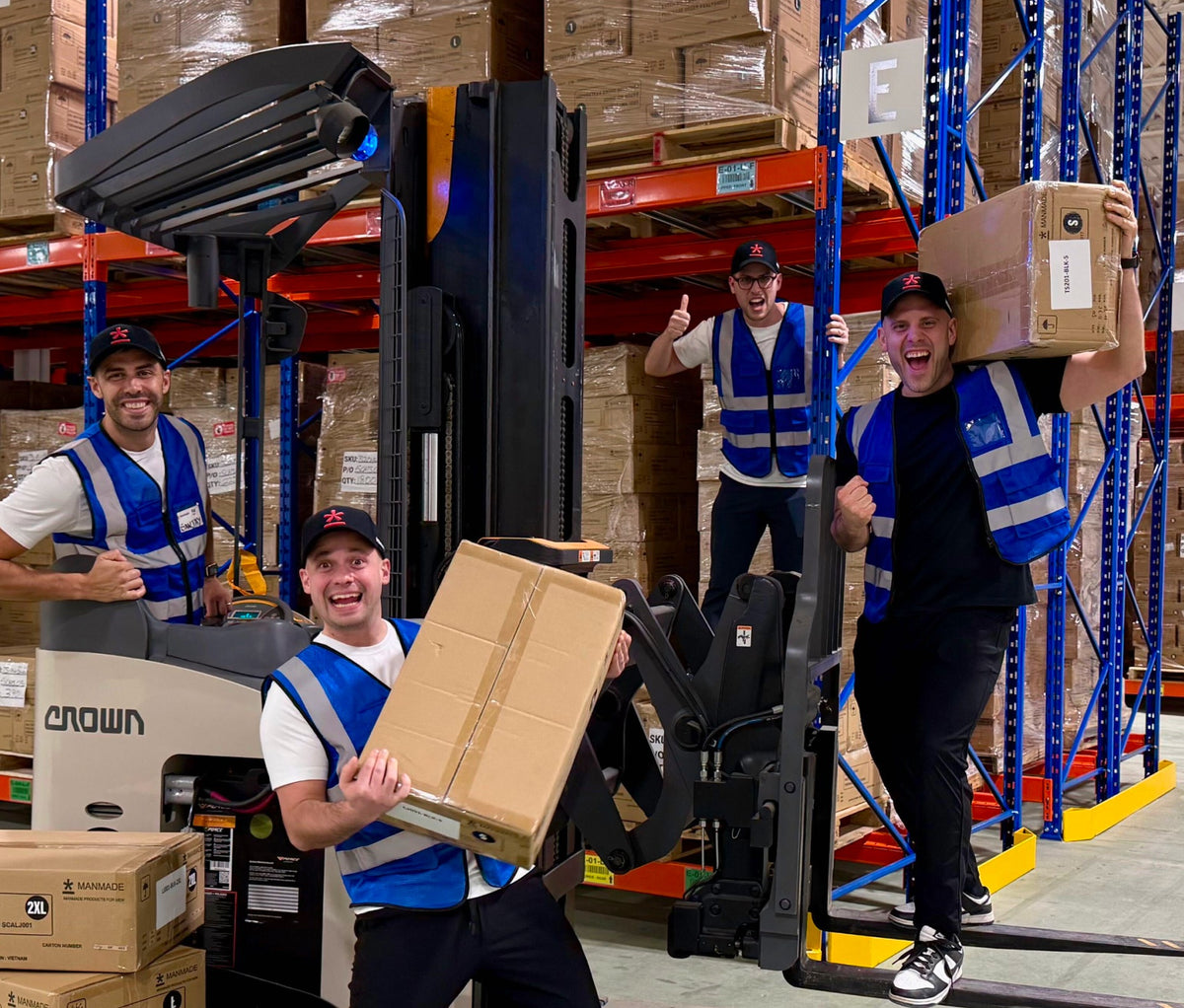 Anthony, Berto, Phil and Rob in blue high-visibility vests work around a forklift in the Manmade warehouse.